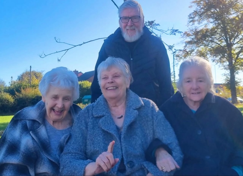 a group of residents sat outside together with warm coats on smiling