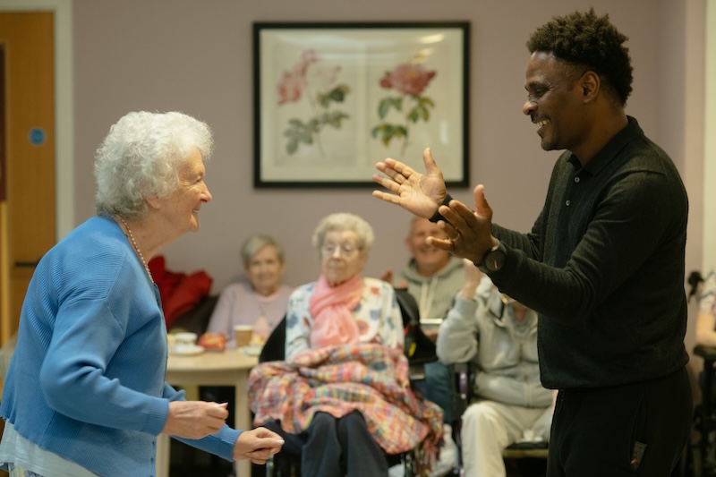 female resident stood up smiling with a carer