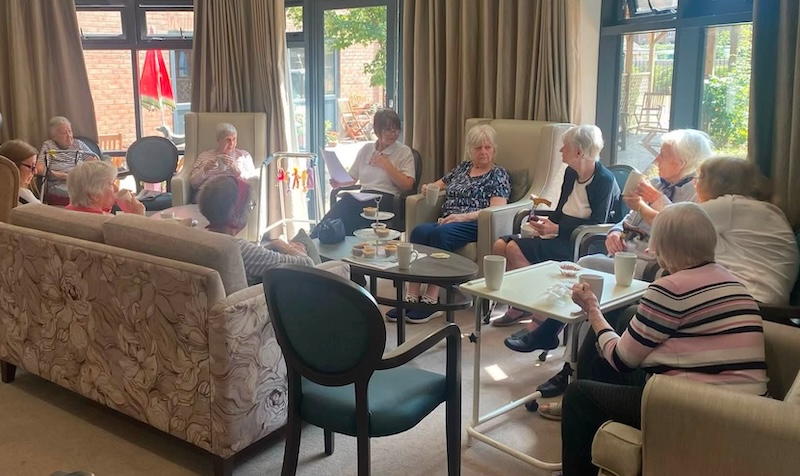 residents all sat down together in armchairs chatting and enjoying snacks